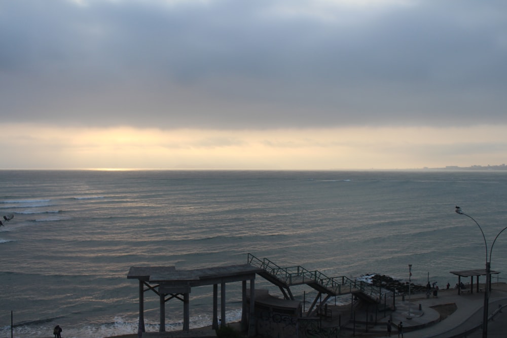 a cloudy sky over the ocean with a pier in the foreground