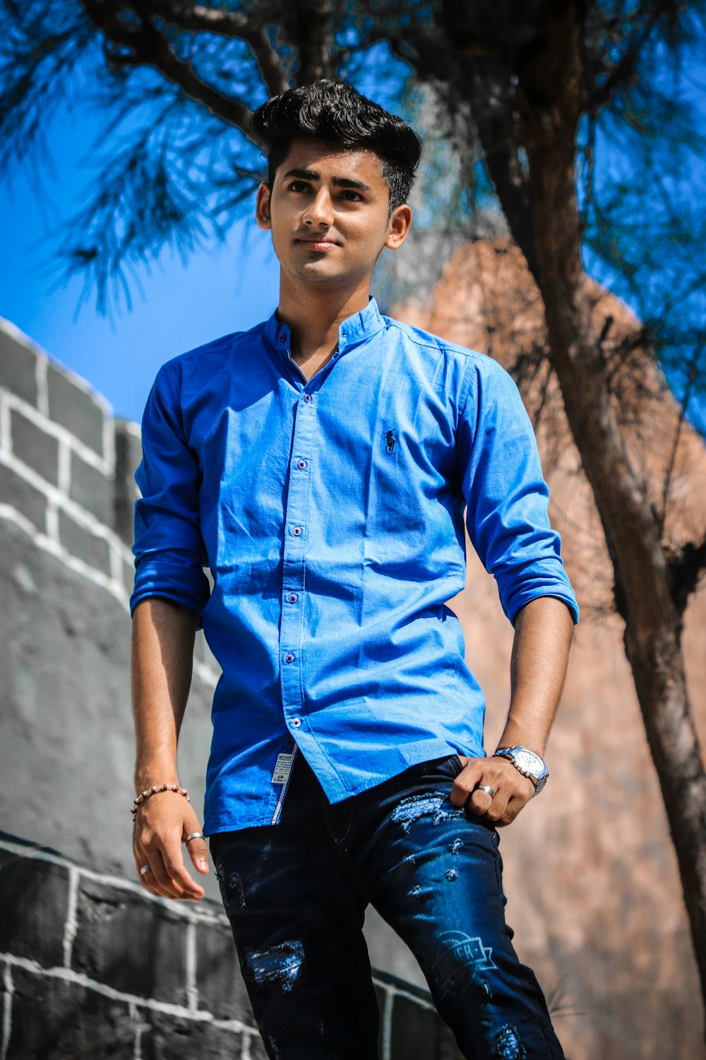 a man in a blue shirt and jeans leaning against a wall