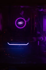 A dimly lit computer interior showcasing a purple LED-lit CPU cooler labeled 'Deep Cool' and a visible GeForce GTX graphics card with blue lighting. The components are encased within a dark chassis and connected with cables.