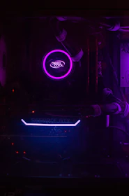 A dimly lit computer interior showcasing a purple LED-lit CPU cooler labeled 'Deep Cool' and a visible GeForce GTX graphics card with blue lighting. The components are encased within a dark chassis and connected with cables.