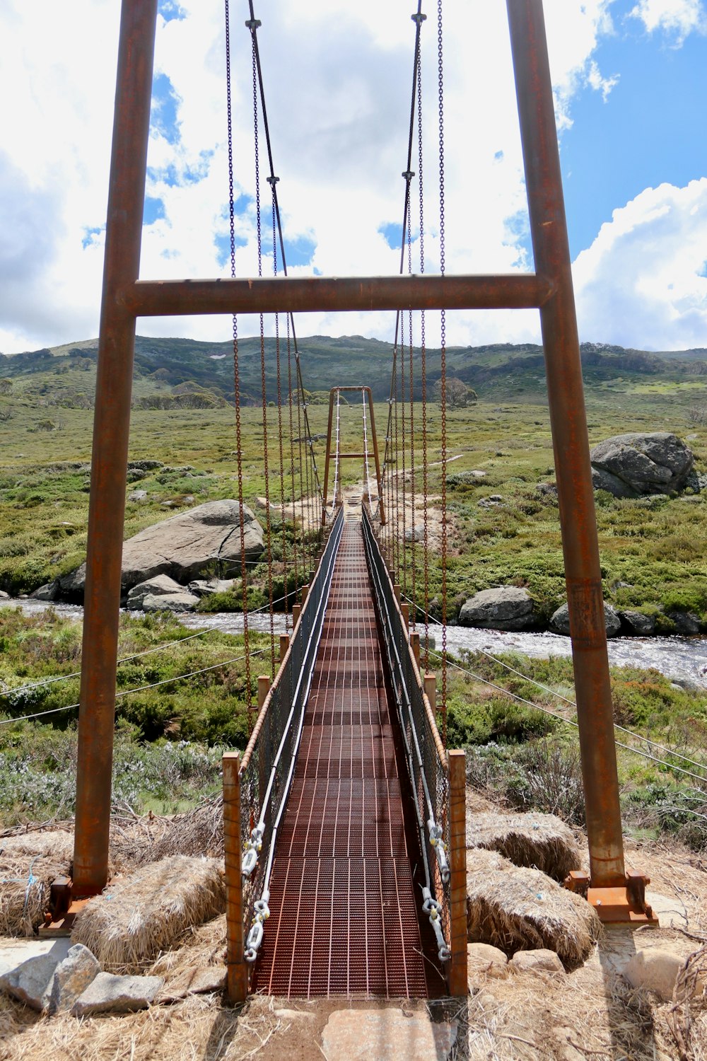 a wooden suspension bridge over a stream in the mountains