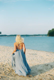 a woman in a blue dress walking on a beach