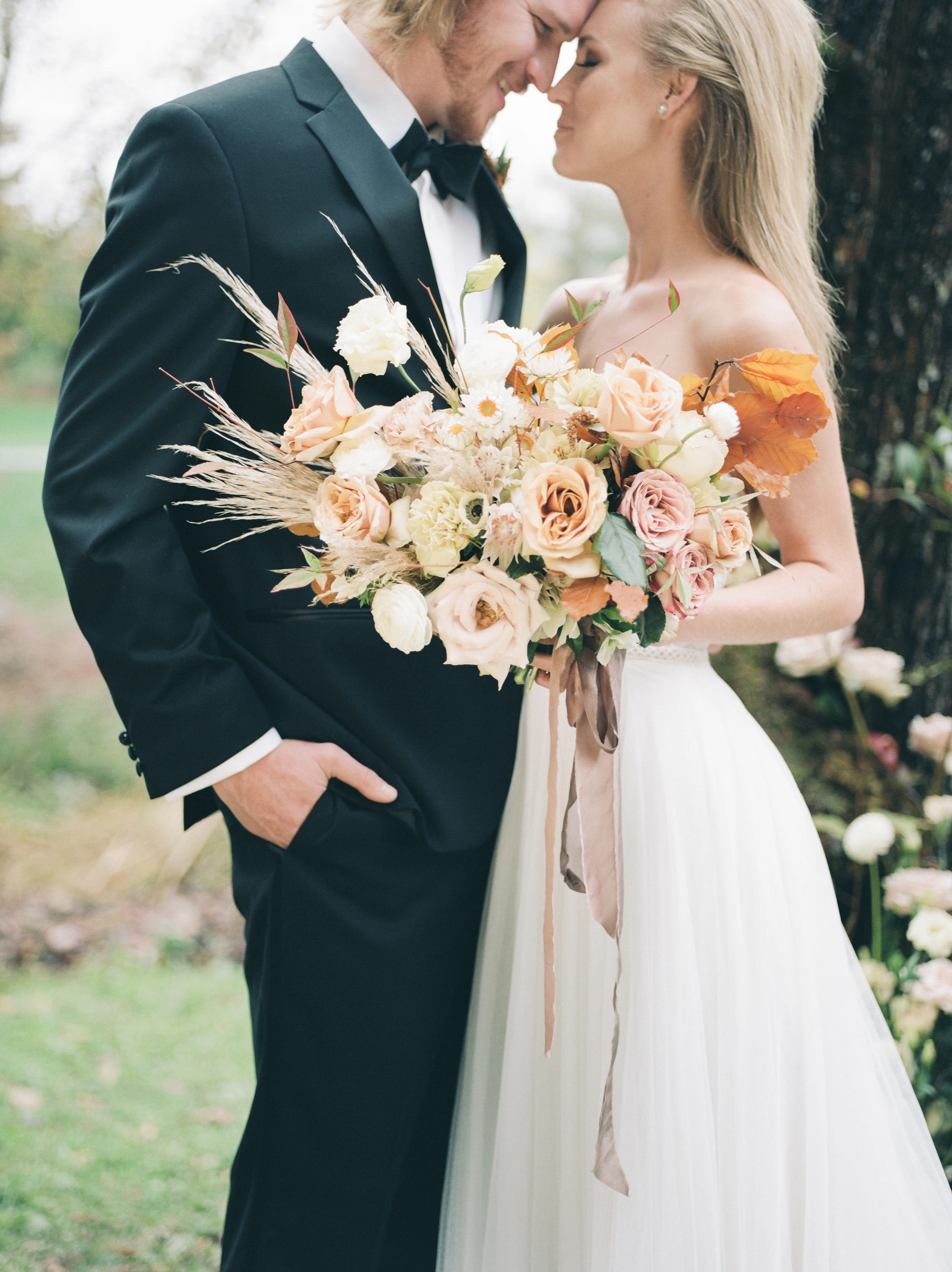 A bride and groom with a dried-flower bouquet beneath a tree