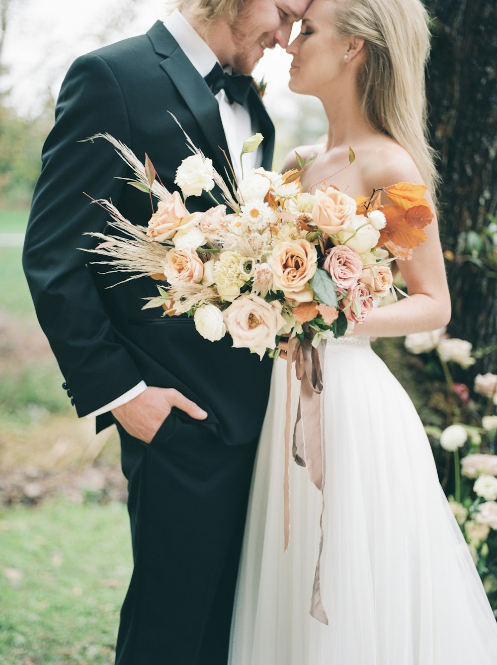 a bride and groom standing in front of a tree