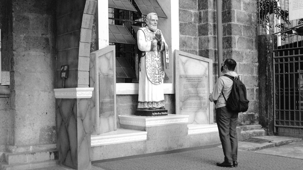 a black and white photo of a man standing in front of a statue