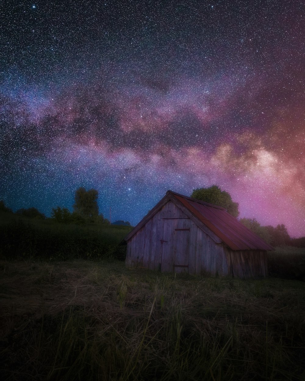 a barn in a field under a night sky filled with stars