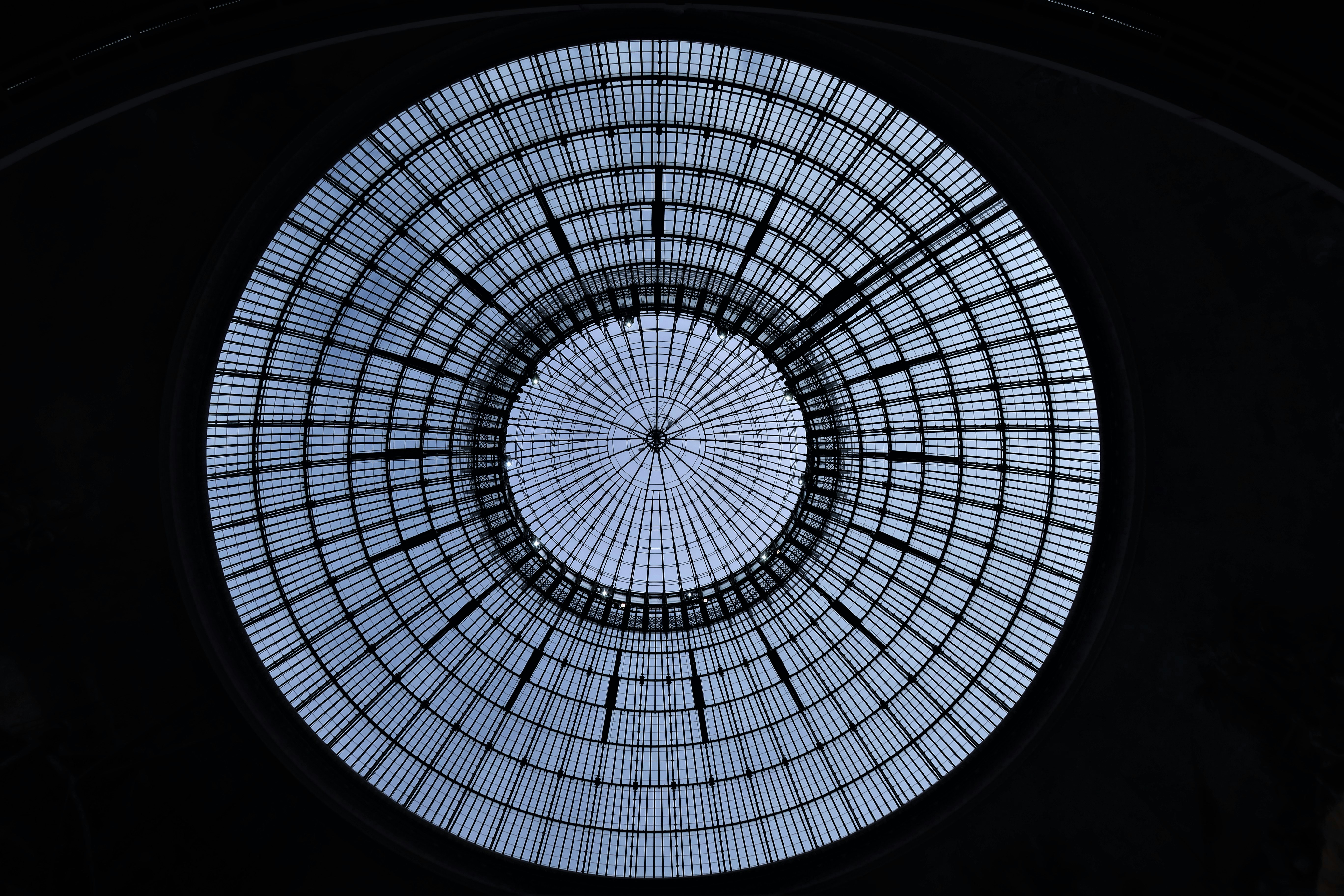 Glass domed ceiling of the Bourse de Commerce commodities market in Paris. It is circular with an intricate array of radiating support bars.