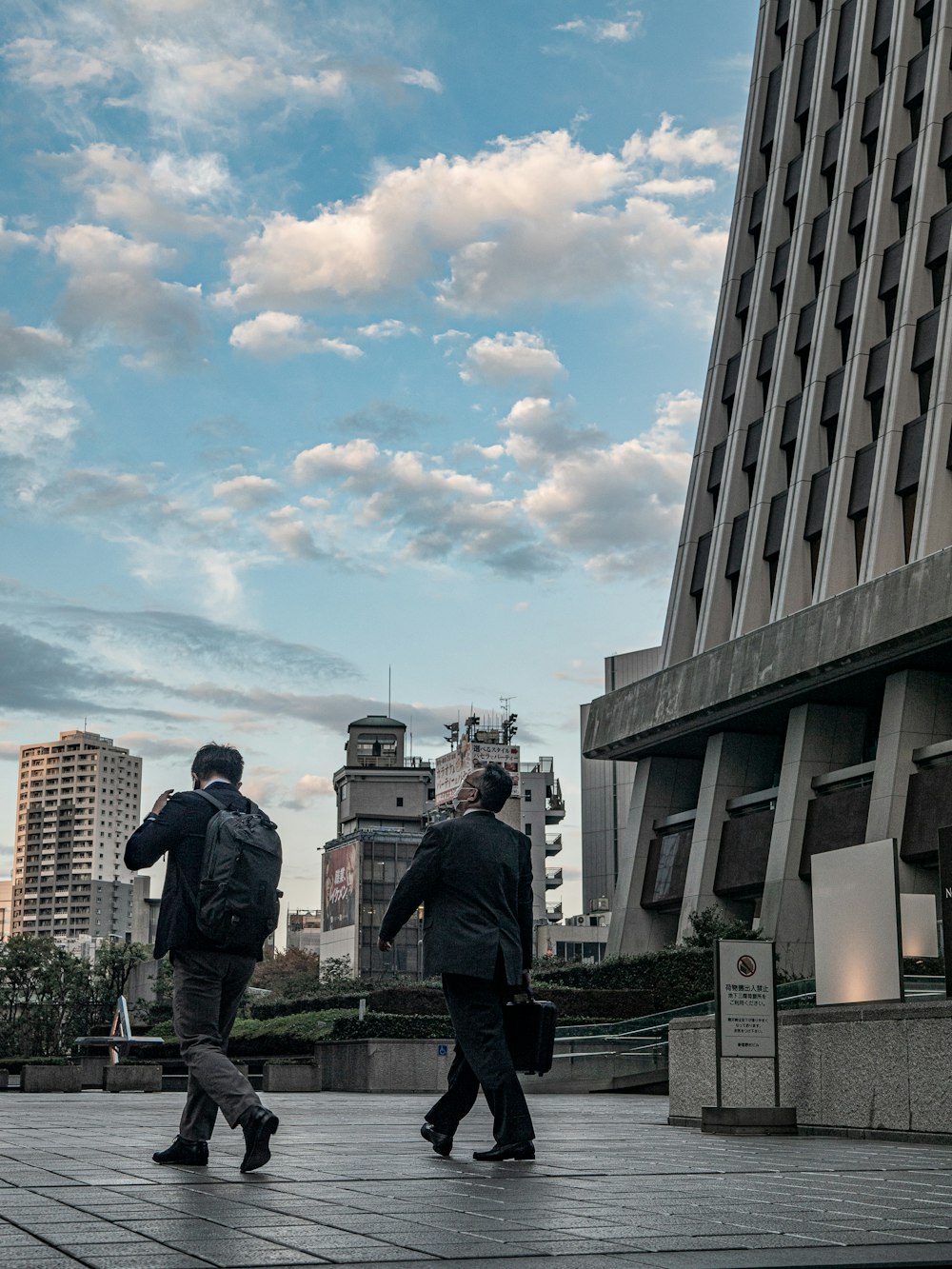 a couple of men walking down a sidewalk next to a tall building