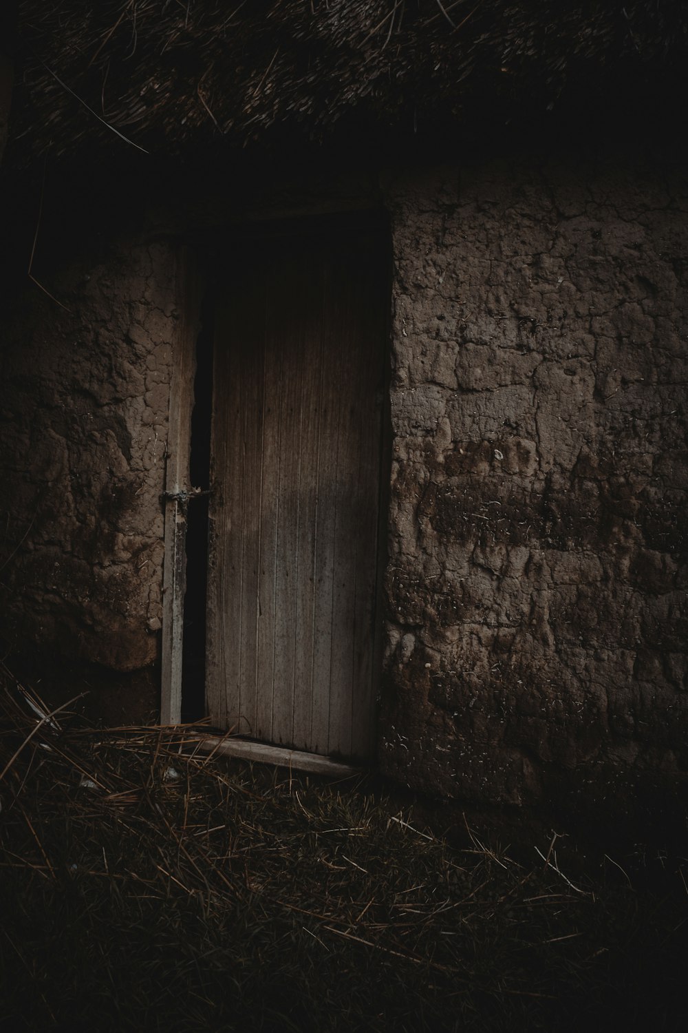 a door in a stone building with straw on the ground