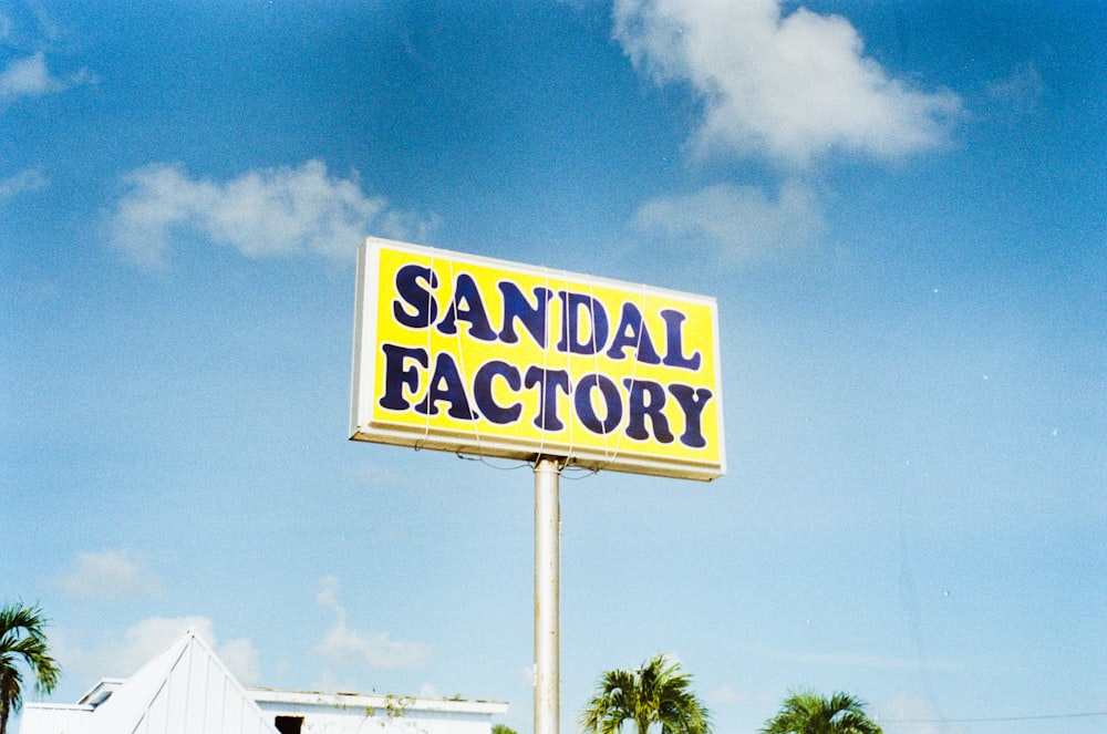 uma placa que diz fábrica de sandálias com palmeiras ao fundo
