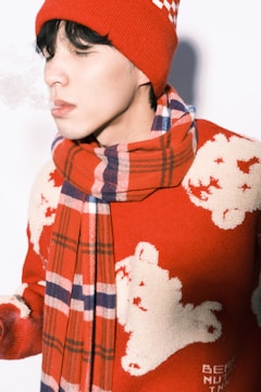 A person is exhaling visible vapor in cold air, wearing a red knit hat and a matching scarf. The sweater features white polar bears on a red background, creating a cozy and festive winter look.