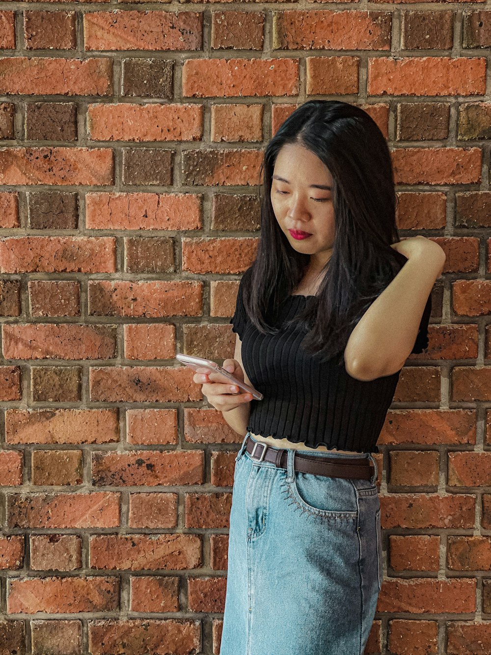 a woman leaning against a brick wall looking at her cell phone
