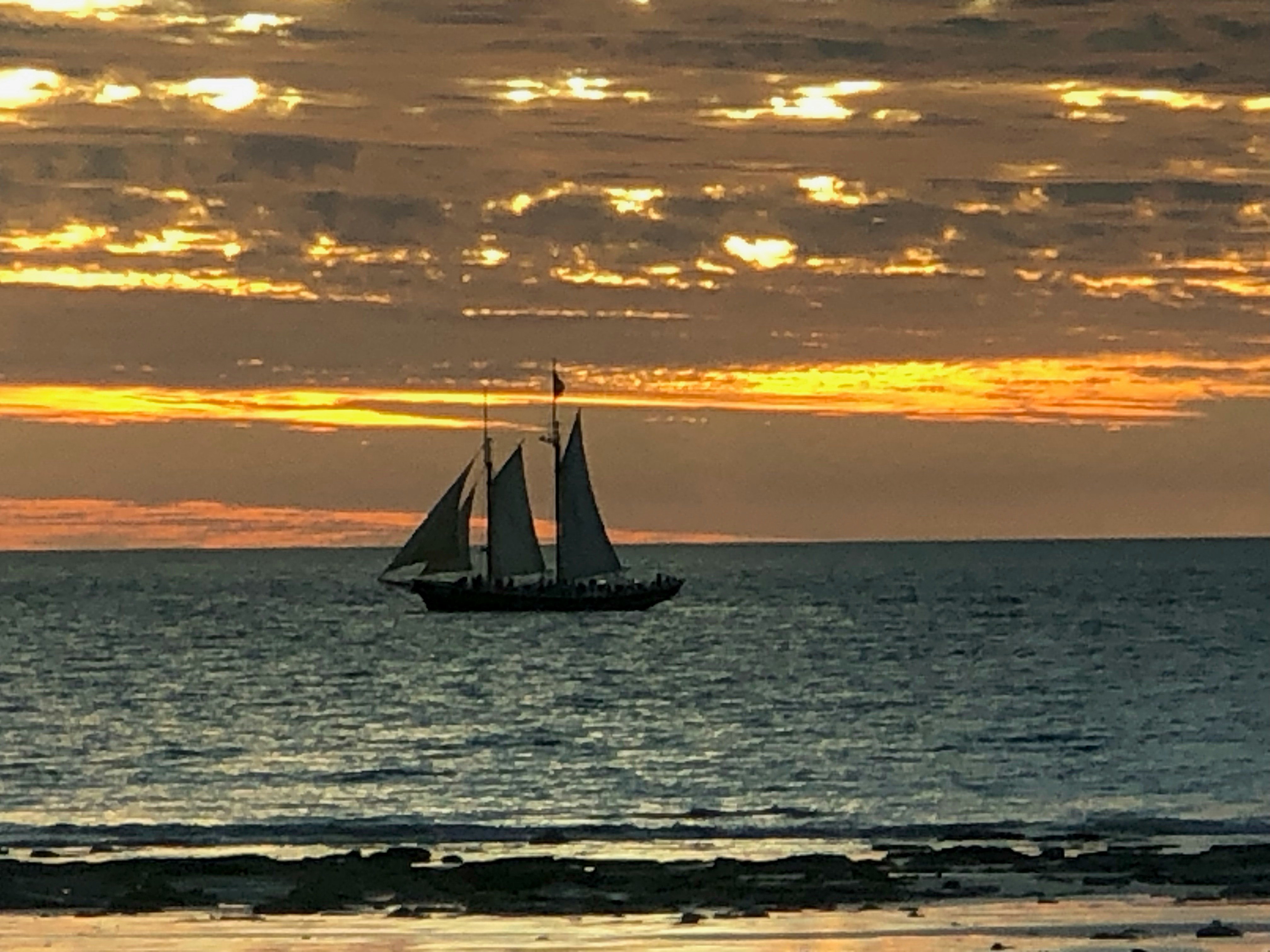 Vista aérea de veleiro navegando em oceano azul profundo ao pôr do sol, horizonte dourado