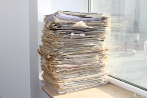 a stack of newspapers sitting on top of a window sill