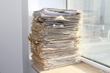a stack of newspapers sitting on top of a window sill