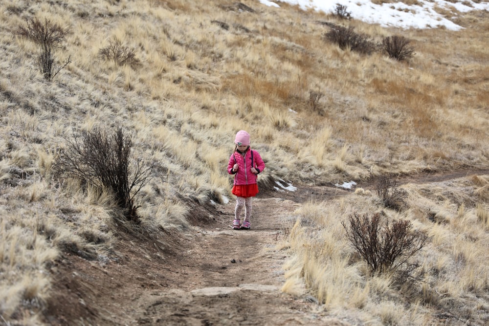 a little girl in a red coat is walking on a trail