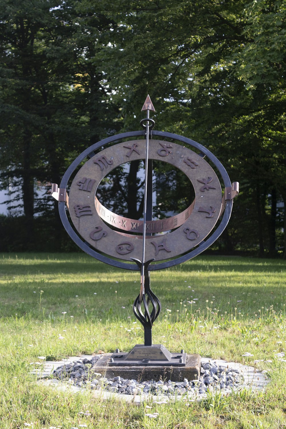 a large metal clock sitting on top of a lush green field