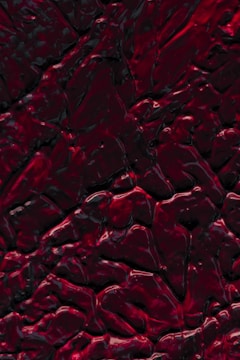 Close-up of a textured dark canvas with streaks of deep crimson and black.