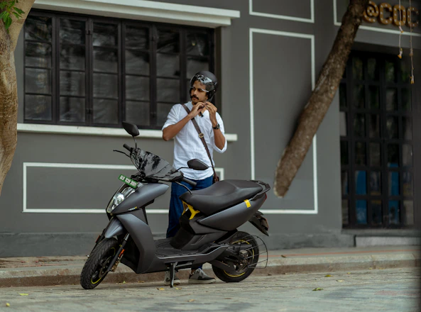 A sleek electric scooter parked by a city sidewalk with a rider putting on a helmet.