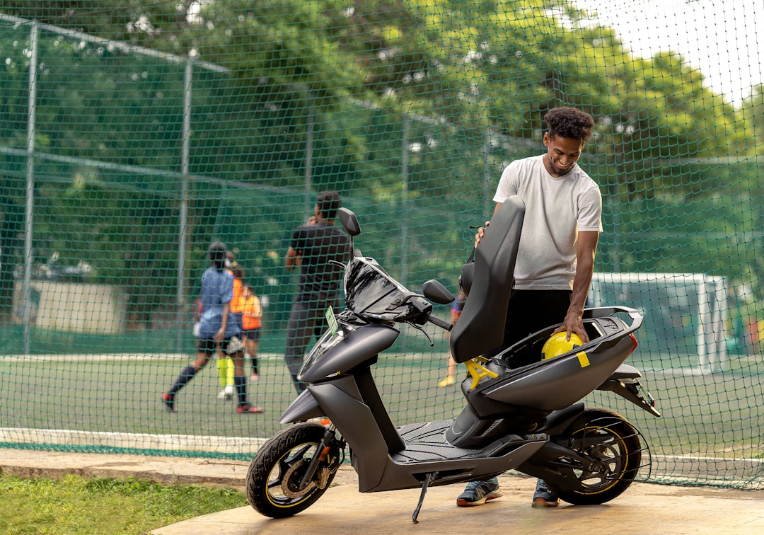 a man standing next to a black scooter, There
