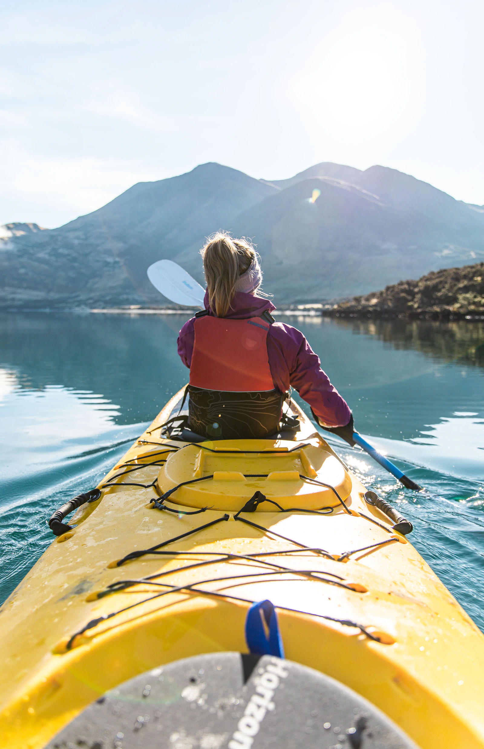 A real kayaker paddling a yellow kayak across clear mountain water