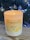 A lit Verzenay Bin 32 hand-poured soy candle is situated on a wooden surface. In the background, a Christmas tree adorned with silver baubles and glowing lights adds a festive atmosphere.
