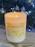 A lit Verzenay Bin 32 hand-poured soy candle is situated on a wooden surface. In the background, a Christmas tree adorned with silver baubles and glowing lights adds a festive atmosphere.