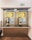 A pair of public payphones are mounted on a wall inside an enclosed booth with glass panels. The payphones offer options for swiping a card or inserting coins to make calls. Above, there are instructions and advertisements for international phone calls. A green emergency exit sign is visible on the wall.