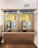 A pair of public payphones are mounted on a wall inside an enclosed booth with glass panels. The payphones offer options for swiping a card or inserting coins to make calls. Above, there are instructions and advertisements for international phone calls. A green emergency exit sign is visible on the wall.