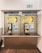 A pair of public payphones are mounted on a wall inside an enclosed booth with glass panels. The payphones offer options for swiping a card or inserting coins to make calls. Above, there are instructions and advertisements for international phone calls. A green emergency exit sign is visible on the wall.