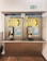 A pair of public payphones are mounted on a wall inside an enclosed booth with glass panels. The payphones offer options for swiping a card or inserting coins to make calls. Above, there are instructions and advertisements for international phone calls. A green emergency exit sign is visible on the wall.