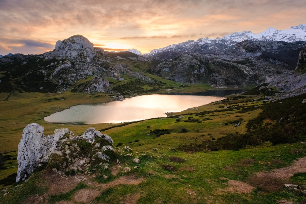 a lake surrounded by mountains with a sunset in the background