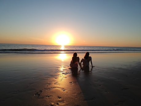 a couple of people sitting on top of a sandy beach