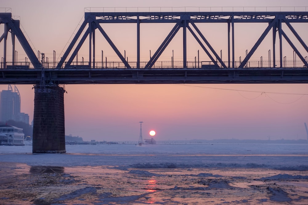 the sun is setting over the water under a bridge