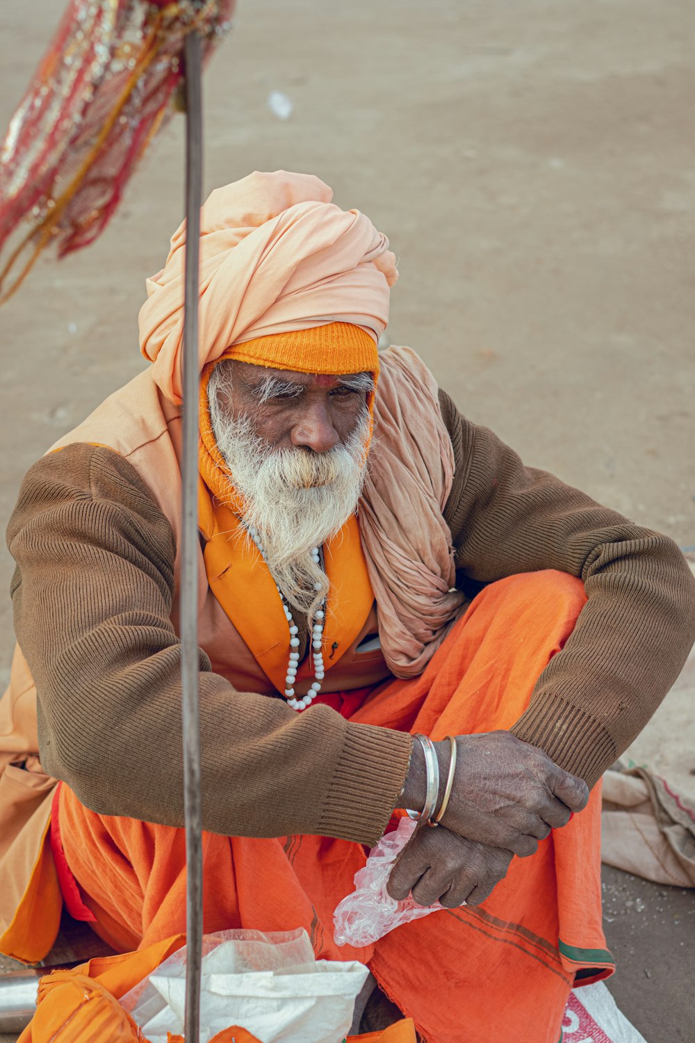 um homem com barba branca e turbante laranja sentado no chão