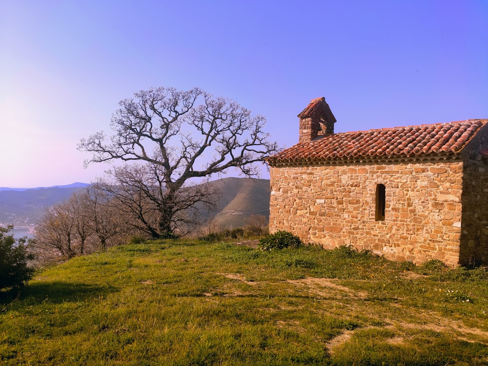 a stone building on a hill with a tree in the background
