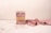 A set of pink cloth towels is neatly folded with a minimalist label attached, placed on a light surface. The cloth extends to the right in a gentle wave pattern. Soft, warm lighting casts gentle shadows, creating a relaxed atmosphere.