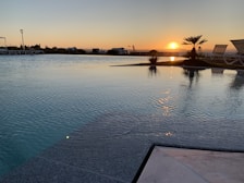 Infinity pool reflecting the vibrant colors of the sunset, surrounded by comfortable lounge chairs.