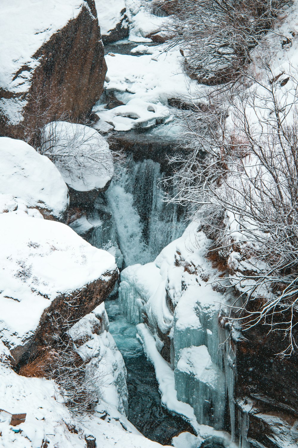 Ein kleiner Wasserfall ist von schneebedeckten Felsen umgeben