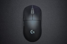 A sleek black gaming mouse with a matte finish and a central scroll wheel, featuring a logo near the bottom, positioned against a dark background.