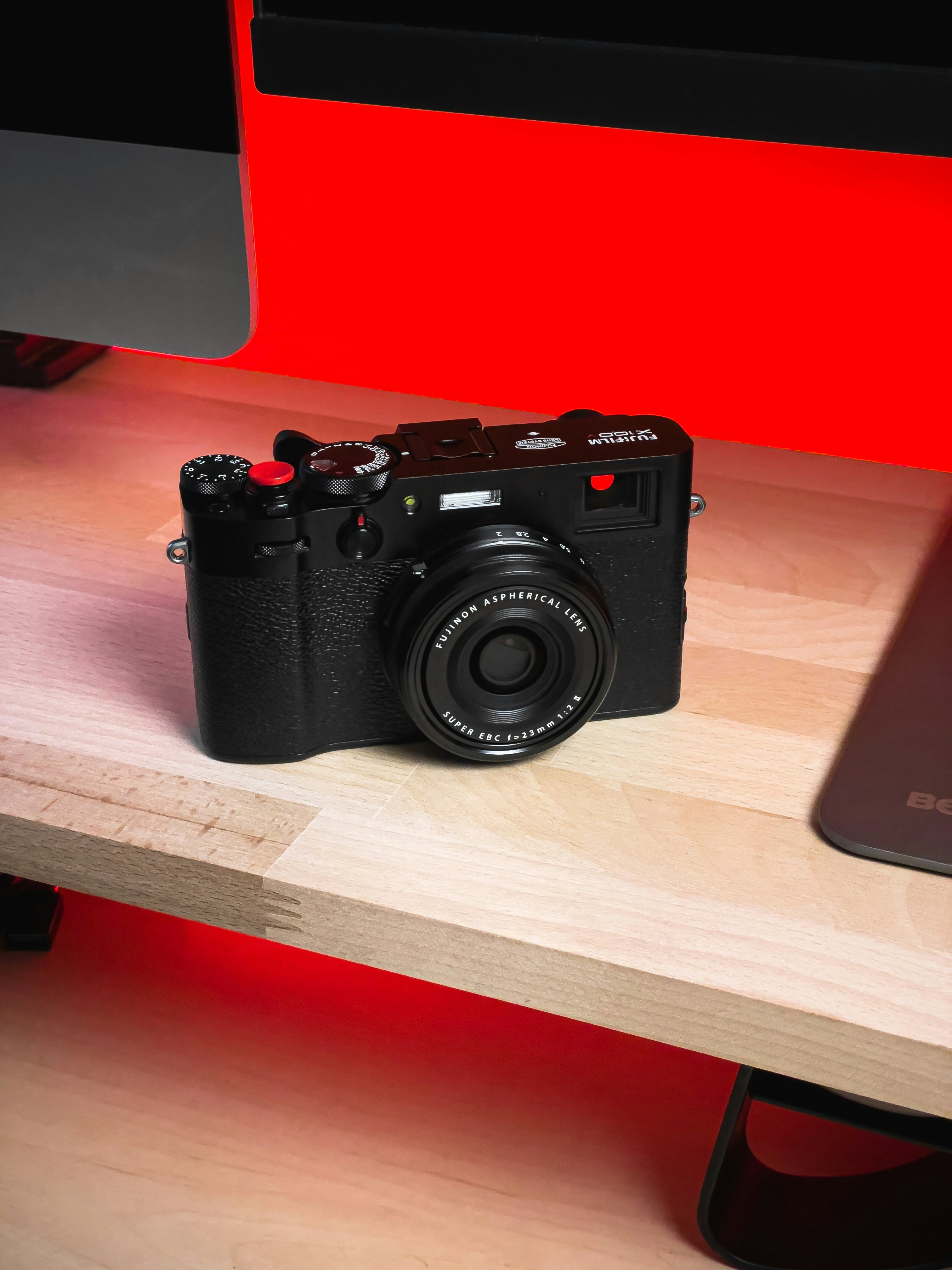 A black digital camera rests on a wooden desk.