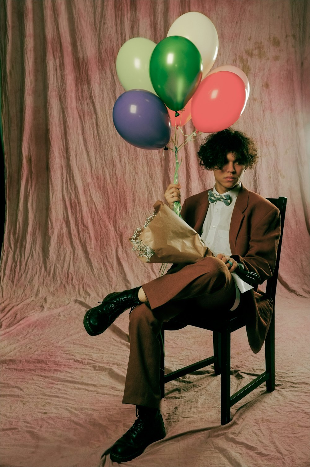 a man sitting in a chair holding a bunch of balloons