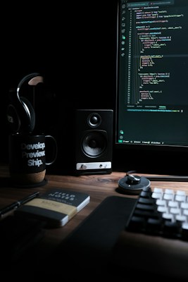 Espacio de trabajo de desarrollo con monitor mostrando código, altavoz y taza con mensaje inspirador