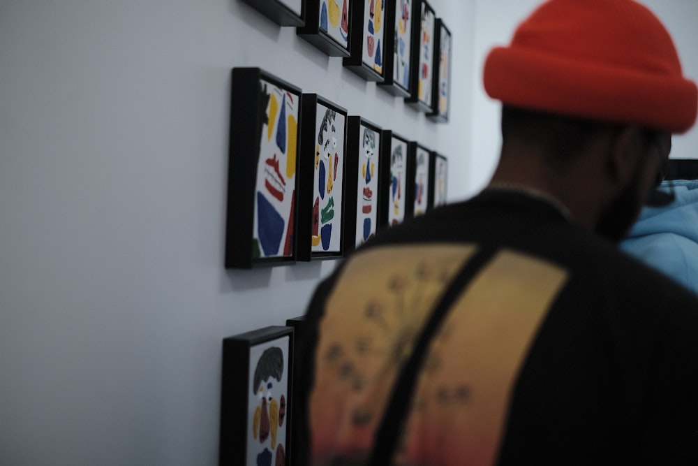 a man wearing a red hat looking at a wall with pictures on it