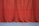 A long red curtain extends from ceiling to floor, creating a rich and dramatic backdrop. The surface of the curtain has subtle folds and drapes that give it texture. The floor beneath is a smooth blue with two painted lines, one red and one yellow, suggesting a sports or auditorium setting.