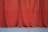 A long red curtain extends from ceiling to floor, creating a rich and dramatic backdrop. The surface of the curtain has subtle folds and drapes that give it texture. The floor beneath is a smooth blue with two painted lines, one red and one yellow, suggesting a sports or auditorium setting.