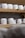 Several rounds of cheese with a textured, white exterior are arranged on wooden shelves. The shelves are part of a storage or aging room.