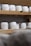 Several rounds of cheese with a textured, white exterior are arranged on wooden shelves. The shelves are part of a storage or aging room.