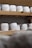 Several rounds of cheese with a textured, white exterior are arranged on wooden shelves. The shelves are part of a storage or aging room.