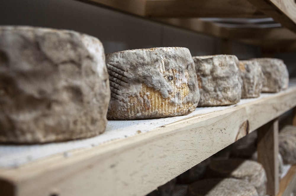 a row of cheeses sitting on top of a wooden shelf